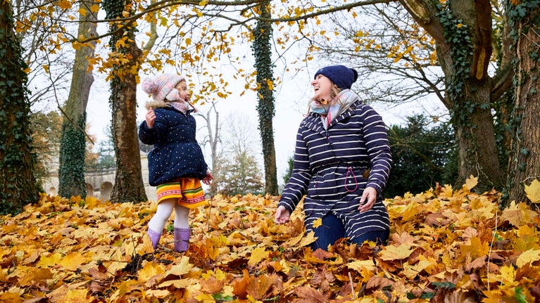 A child and lady wrapped up warm, playing in autumn leaves